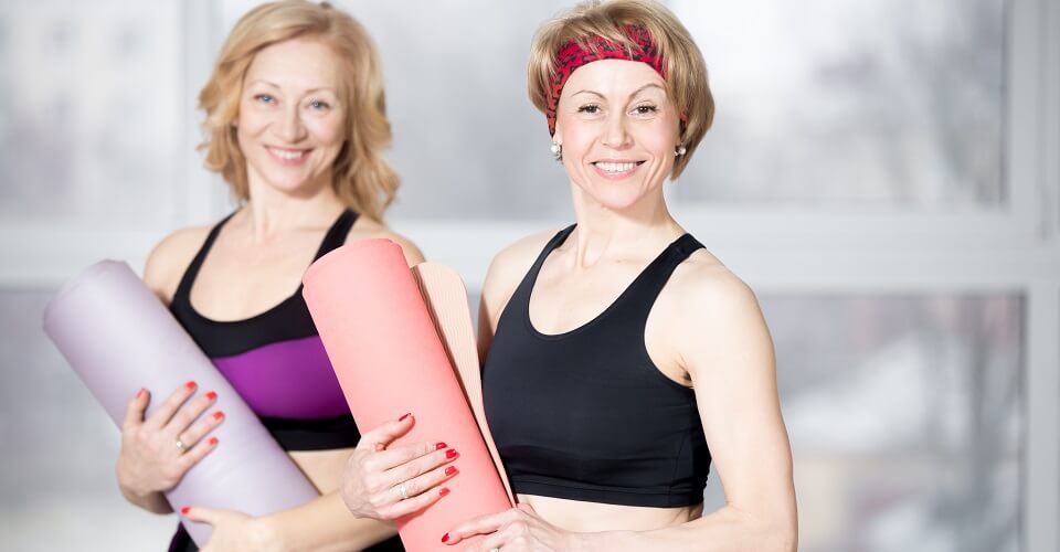 2 older women holding a yoga mat and smiling