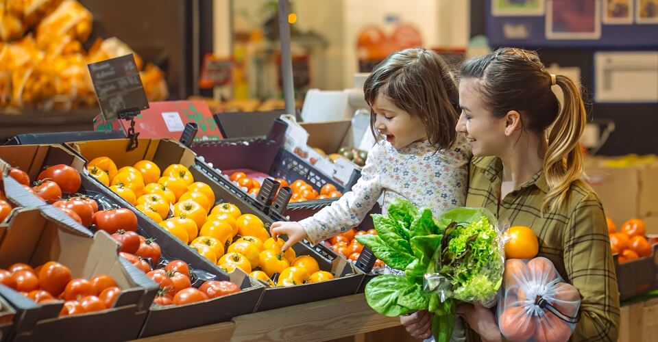 Family in the supermarket. Beautiful young mom and her little daughter smiling and buying food. The concept of healthy eating. Harvest