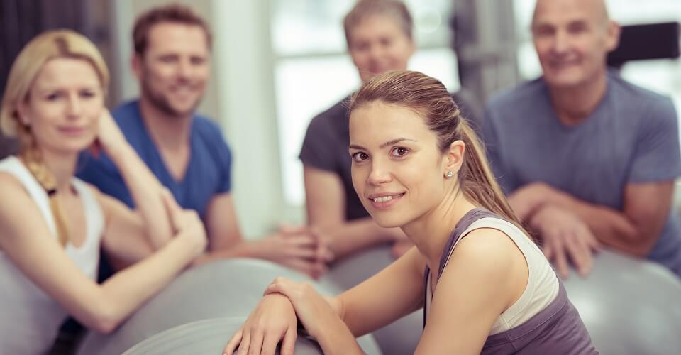 Group of diverse young and old people in a pilates class at the gym with focus to an attractive young woman in the foreground in a health and fitness concept