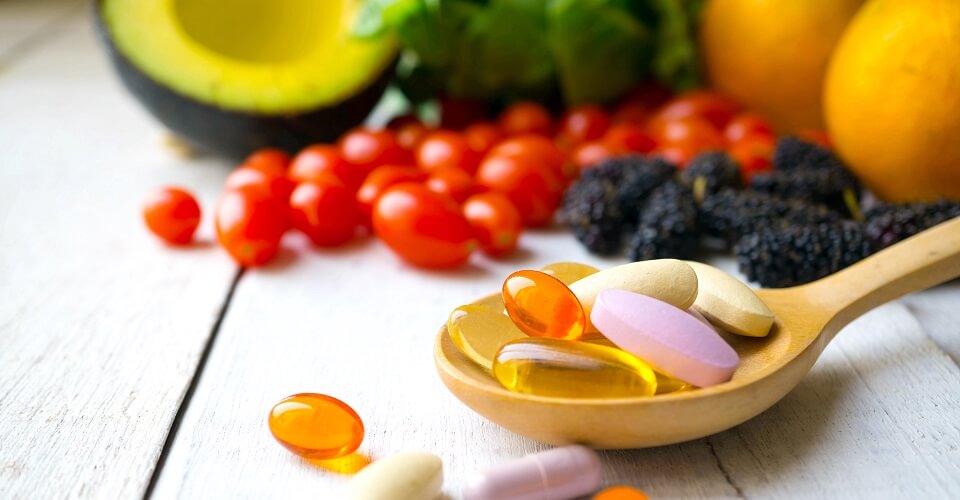 Pills and capsules in wooden spoon with fresh fruits.Multivitamins and supplement from fruits concept.