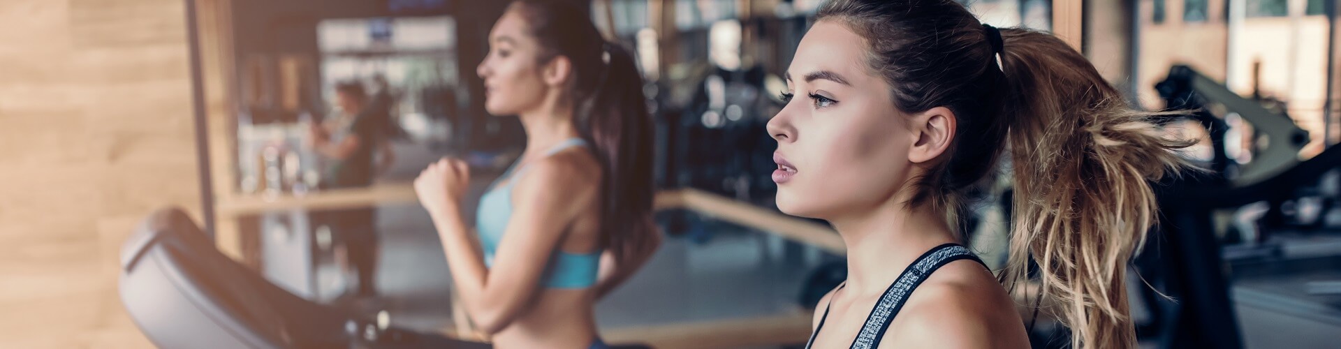Side view of two attractive sports women on running track. Girls on treadmill